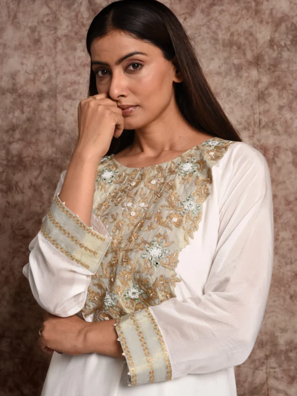 Close-up portrait view of Verbena suit top detailing gold threadwork bib neckline and embroidered cuff sleeve borders by Embrowhite