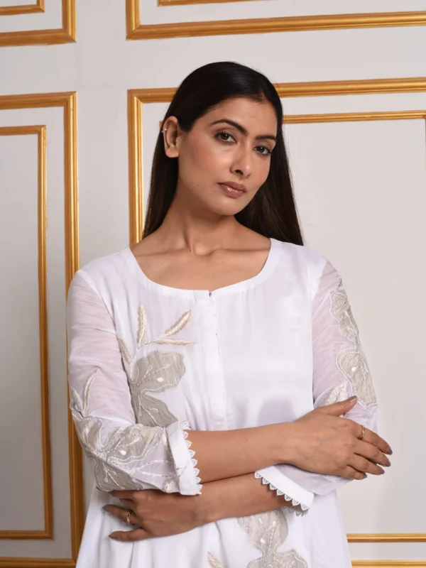 Close-up view of woman wearing white Pastel Mosaic co-ord set top with subtle gold floral embroidery and lace cuffs