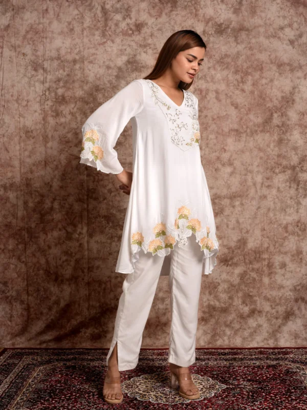 Side angle view highlighting scalloped floral cutwork hemline and side-slit trousers on Zora white tunic set by Embrowhite